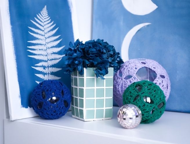 Vase mosaïque terminé, exposé avec des décorations faites main et des fleurs.