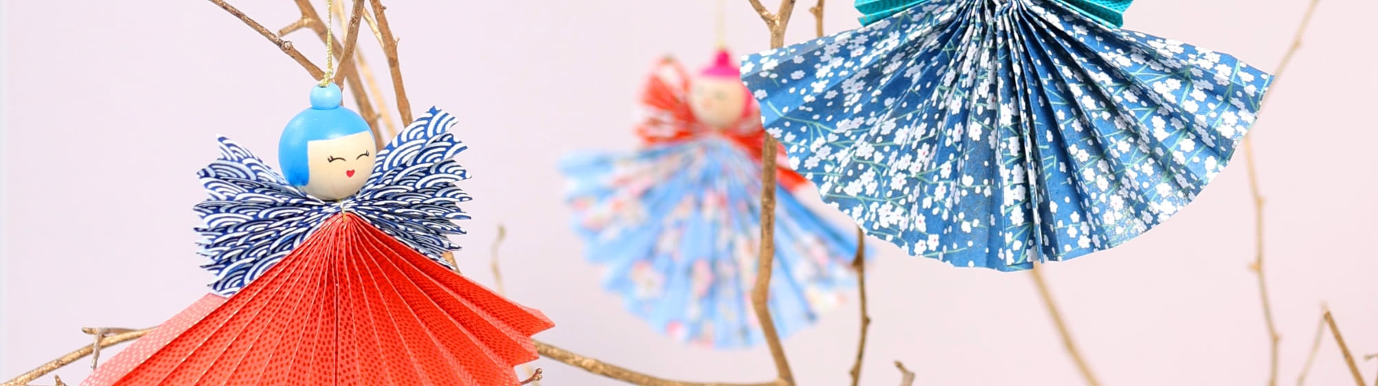 Anges en papier devant des branches sur fond rose