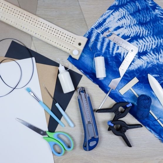 Matériel nécessaire pour la fabrication du carnet : outils de reliure, ciseaux, colle et tissu cyanotype.