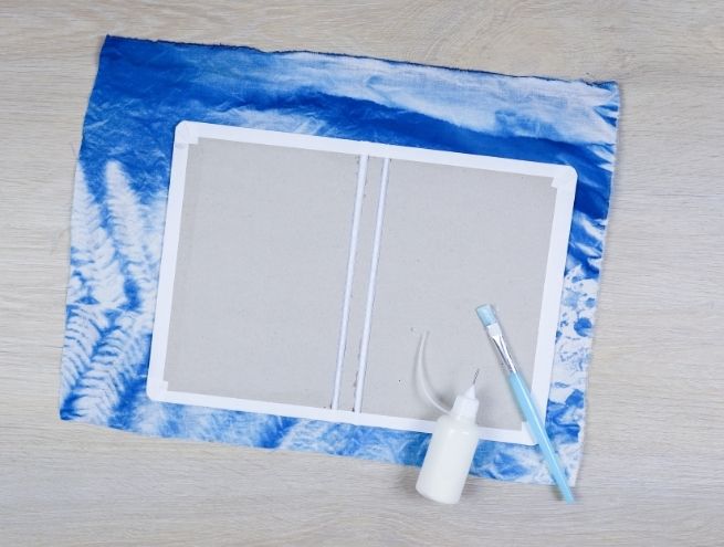 Première étape du tutoriel reliure : collage du carton sur le tissu cyanotype bleu.