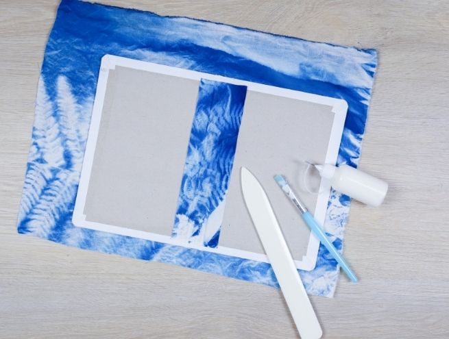 Étape de fabrication du carnet : pliage et collage des rebords du tissu cyanotype.