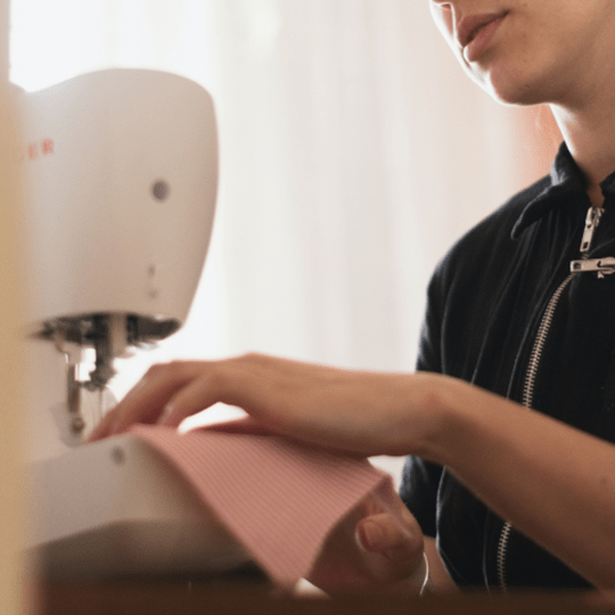 Une femme est en train de coudre un tissu avec une machine à coudre. Zoom sur sa main. 