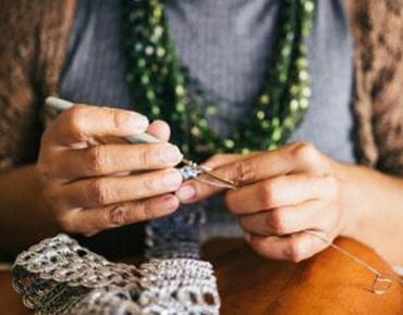 Mains en train de crocheter avec un fil métallisé argenté, sur une table en bois.