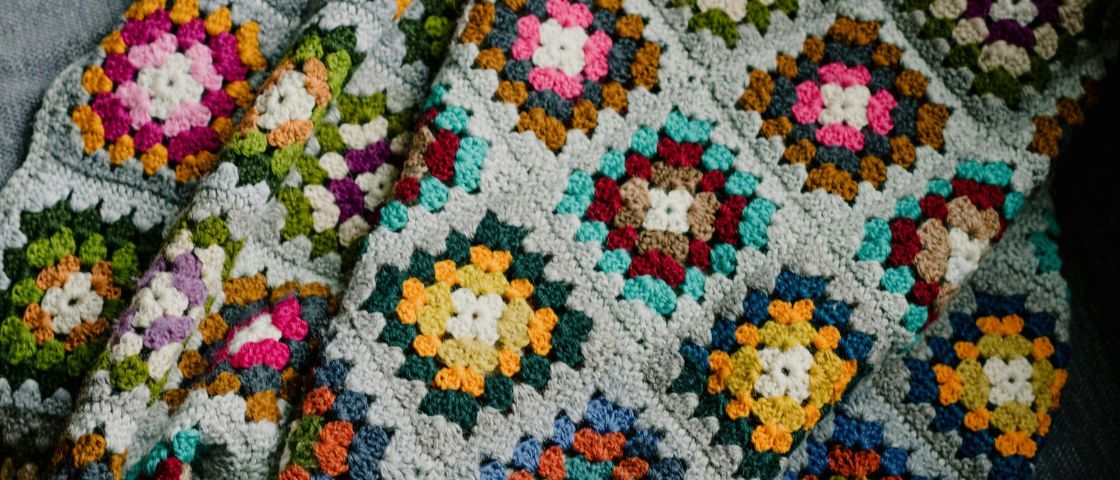 Plaid en granny squares colorés avec un fond gris, réalisé au crochet.