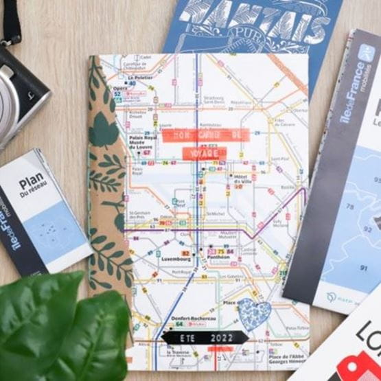 Carnet de voyage personnalisé posé sur un plan de métro parisien, entouré de guides et d’accessoires touristiques.