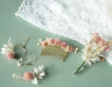 Ensemble de bijoux et accessoires en fleurs séchées, comprenant boucles d’oreilles, peigne et boutonnière, sur fond vert.